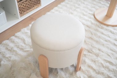 Yuvarlak bir tabure, temiz dekorlu basit bir odada, halının üzerinde oturur..