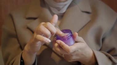 Bir insan evde otururken küçük bir kavanozdan krema kullanıyor..