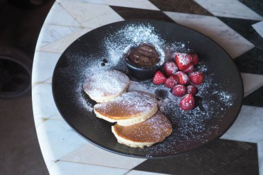 Çikolata ve çilekli siyah bir tabakta üç krep..