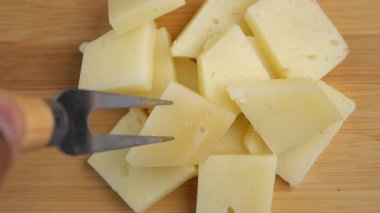 Slices of cheese are cut into small pieces using a fork.