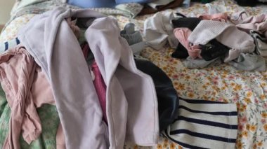 Kıyafetler düzenlenmek için sıralanması ve katlanması gereken bir yatağa saçılmış..