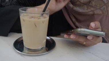 Birisi kafede telefon kullanırken buzlu içeceğini yudumluyor..