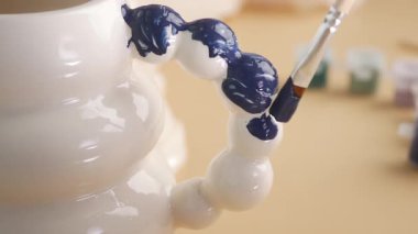 Kişi mavi detaylar ve desenlerle seramik bir kupa çizer.