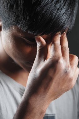 Genç bir adam yalnız duruyor, alnına dokunuyor, stresli görünüyor..