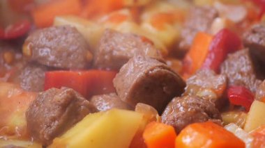 Et ve çeşitli sebzeler tencerede kaynayarak sıcak bir yemek oluşturur..