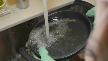 Birisi mutfak lavabosunda akan suyun altında siyah bir tavayı duruluyor..