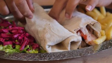 Bir insan masada patates kızartması ve salatayla otururken shawarma sarar..