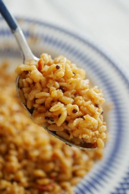 Bir kaşık pirinci yanında daha fazla pirinçle mavi ve beyaz bir tabakta servis eder..