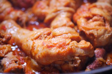 Tavuk parçaları baharatlı ve soslu bir tencerede yavaş yavaş pişiyor..
