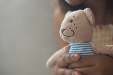 A child hugs a teddy bear while sitting in a quiet room, smiling softly.