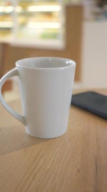 Beyaz bir kupa ahşap bir masada telefonun yanında oturuyor..