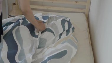 Kişi, basit bir yatak odasındaki yatağa yorgan koyuyor..