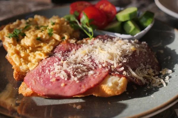 Sıcak bir kahvaltı tabağında çırpılmış yumurta, et ve dilimlenmiş sebze var..