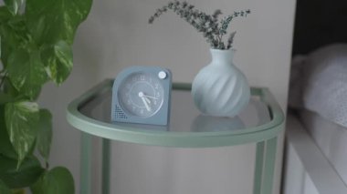 Bir saat, yatağın yanındaki komodindeki vazonun yanındaki zamanı gösterir..