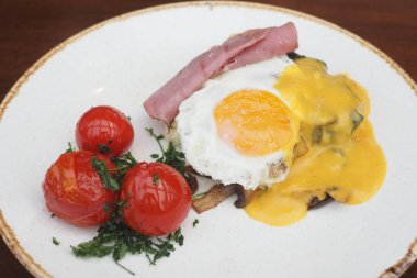 Kızarmış yumurta, dilimlenmiş jambon, domates ve otlarla servis edilir..