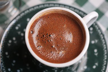 Yeşil desenli masa örtüsü üzerinde bir fincanda sıcak Türk kahvesi..