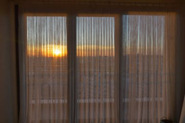 Güneş binaların ötesinde batar, ışık filtreleri perdelerin ardında..