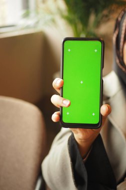 Bir kişi evde otururken yeşil ekranlı akıllı telefonu gösterir.