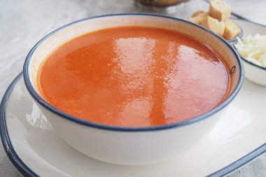 Domates çorbası, yakınlardaki ekmek ve malzemelerle dolu büyük beyaz bir kaseyi doldurur..