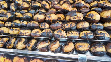 Bir satıcı kalabalık bir pazarda kavrulmuş kestane satıyor. İnsanlar bu yemeği seviyor..