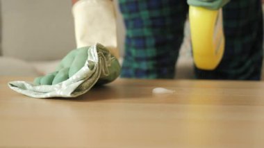 Bir insan ahşap bir masayı bez ve temizlik spreyi kullanarak temizler..