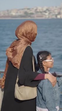 Bir kadın ve kız güneşli bir günde denize bakarlar..