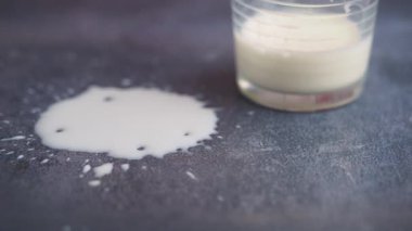 Bir bardak süt yuvarlanır ve bir masa yüzeyine dökülür..