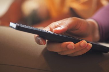 Bir kişi televizyondaki kanalı değiştirmek için uzaktan kumanda kullanıyor.