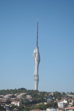 Parlak mavi gökyüzünün altındaki şehir binalarının üzerinde yükselen uzun kule.