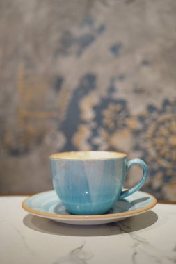 Bir fincan çay tabağı dekoratif bir duvarın önündeki masada duruyor..