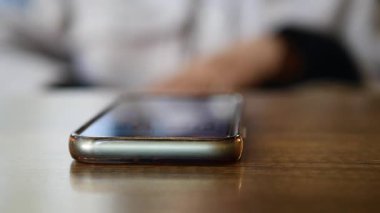 İnsanlar kafenin etrafında dolaşırken bir telefon masanın üzerinde duruyor..