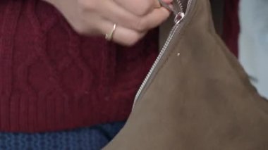 Biri kahverengi bir süet çantanın fermuarını aletlerle onarıyor..