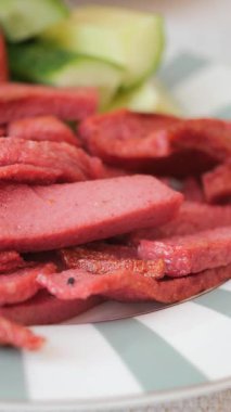 Dilimlenmiş sosis bir tabağa konur salatalık dilimlerinin yanına..