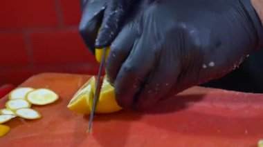 Biri mutfaktaki kırmızı kesme tahtasıyla limon dilimliyor..