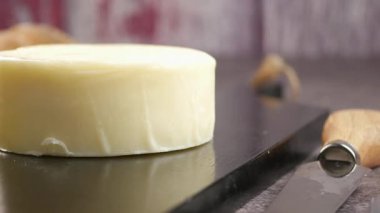 Yuvarlak bir peynir parçası siyah bir taşın üzerinde duruyor. Kesmek için yakında bir bıçak bekliyor..