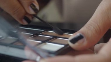 Bir kişi bir paletten göz farı sürmek için bir fırça kullanır.