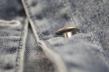 Düğme mavi kot kumaşa bağlanmış. Kıyafet detaylarını gösteriyor..