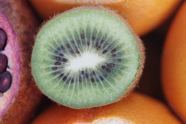 Bir kivi meyvesi diğer meyvelerin yanında içindeki yeşili göstererek ikiye bölünür..