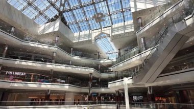 Birden fazla katlı ve cam çatılı bir alışveriş merkezi manzarası.