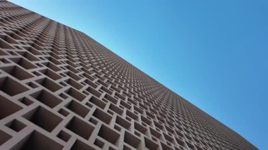 Kamera, üzerinde açık mavi gökyüzü olan yüksek bir binaya bakıyor..