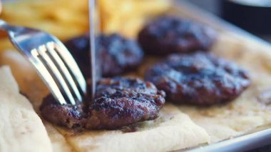 Cutting grill meat on a plate with fork and knife in busy cafe.