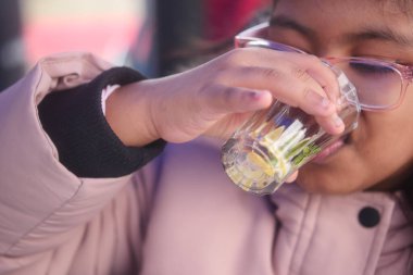 Bir kız, içi temiz sıvıyla dolu küçük bir bardaktan içer..