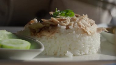 Salatalık dilimleri ve otlarla servis edilen bir tabak pilav ve tavuk..