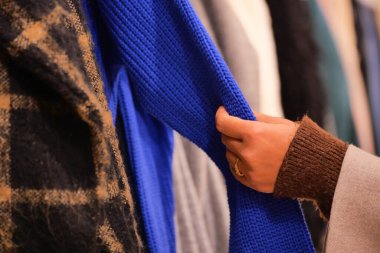 Bir insan mağazadaki bir raftaki kıyafetlere bakıyor..