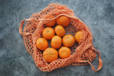 Portakallar gri bir yüzey üzerinde turuncu bir ağ torbasına konur..