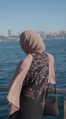 Suyun kenarında duran bir kadın şehrin ufuk çizgisine bakıyor..