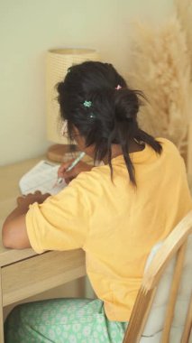 Tahta masada oturan bir kız kalemle notlar yazıyor..