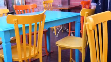 İnsanlar renkli sandalyeleri ve masaları olan bir kafede eğleniyorlar..