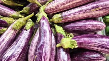 Patlıcanlar bir market tezgahına istiflenmiş. Müşteriler ürünlere bakar..