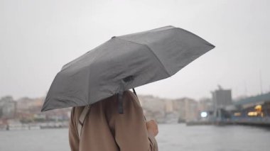 Bir insan yağmur yağarken şehirde su kenarında yürür..